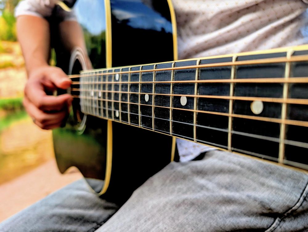 Nahaufnahme: Hand schlägt die Saiten einer schwarzen Akustikgitarre an